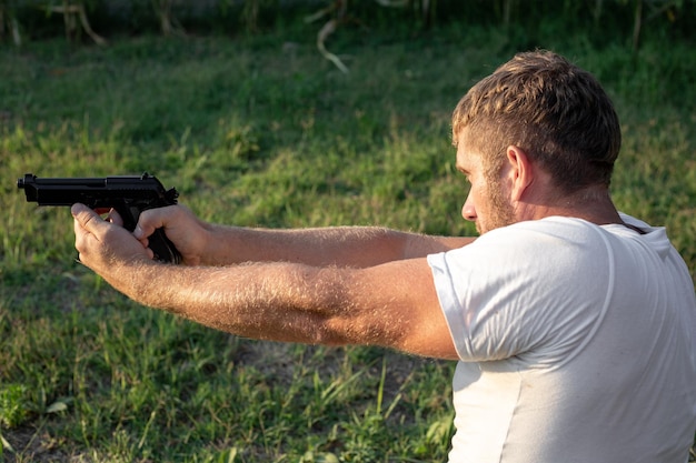 A caucasian man stands and aims a gun on the street on a summer day