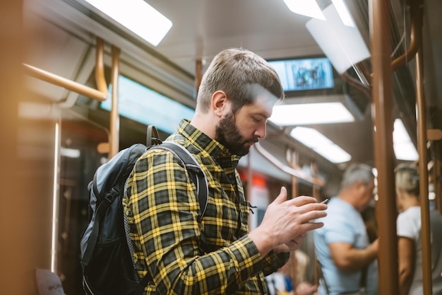 Caucasian man traveling by metro standing in subway car holding mobile telephone in handsImage with selective focus