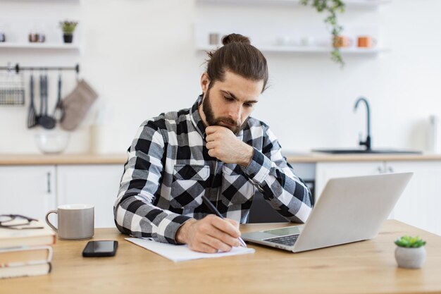 Caucasian man wearing checkered shirt writing on document