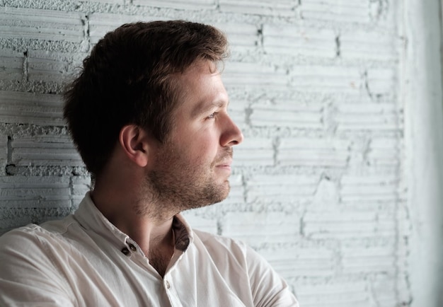 Caucasian man in white shirt standing near wall and smile a little He is content and confident