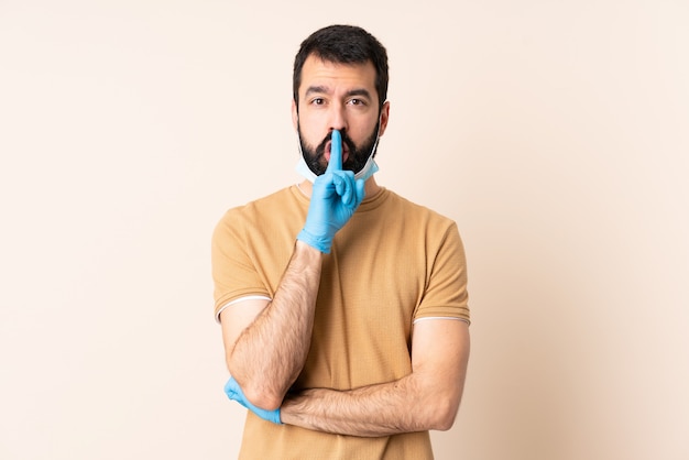 Caucasian man with beard protecting with a mask and gloves over wall showing a sign of silence gesture putting finger in mouth