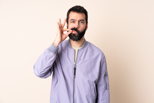 Caucasian man with beard wearing a jacket over wall showing a sign of silence gesture