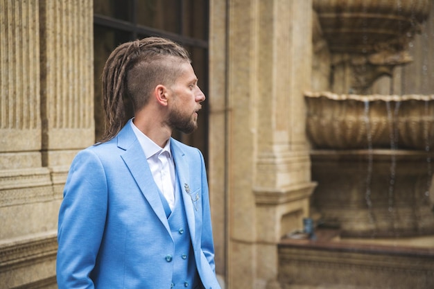 Caucasian man with dreadlocks in blue three piece business suit outdoor portrait