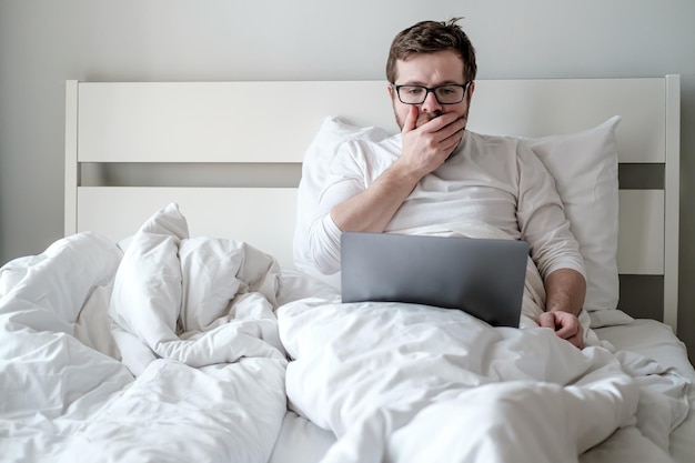 Caucasian man with a laptop in bed received bad news he is scared and upset