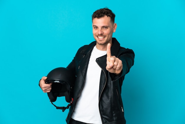 Caucasian man with a motorcycle helmet isolated on blue wall showing and lifting a finger