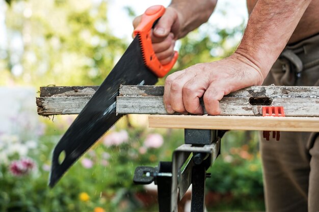 Photo caucasian man working cutting plank with handsaw outdoor in summer