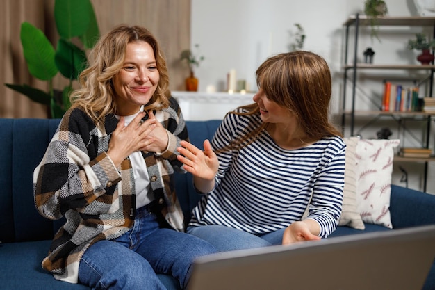 Caucasian mature mother and her adult daughter sitting on sofa in front of laptop