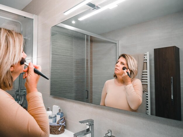 Caucasian mature woman putting makeup on her face