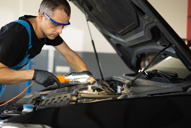 Caucasian mechanic in blue overalls is working on a car in a car service repairman in safety glasses