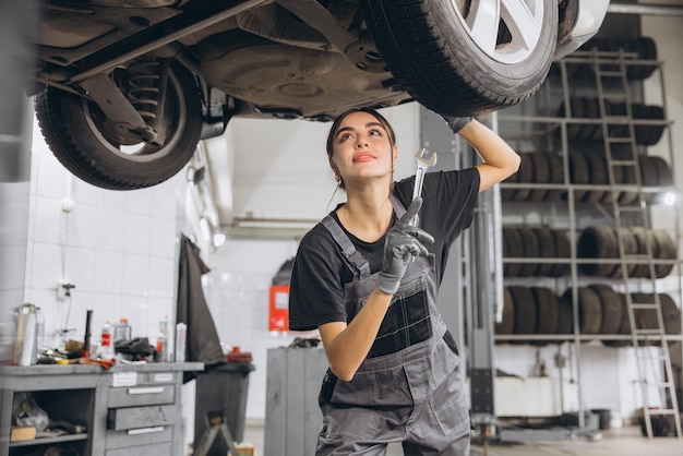 Caucasian mechanic woman fixing underneath car in auto repair shop female worker in grey uniform doing vehicle maintenance in repair garage