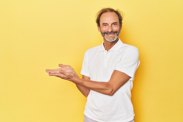 Caucasian middleaged man in yellow studio holding a copy space on a palm