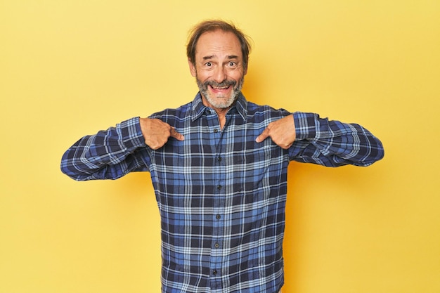 Caucasian middleaged man in yellow studio surprised pointing with finger smiling broadly