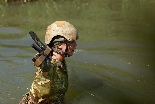 Caucasian Military lady woman in tactical gear posing for photo at summer season Wearing green camo uniform and assault rifle in military gear and headset lady is looking at side