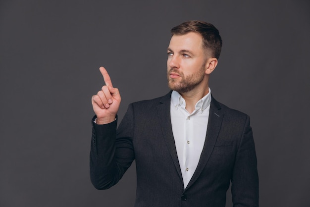 Photo caucasian millennial businessman isolated on gray studio background posing satisfied successful man in formal suit pointing something with finger at copy space