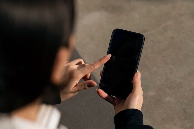 Caucasian millennial lady in headphones typing on smartphone with blank screen outdoor close up