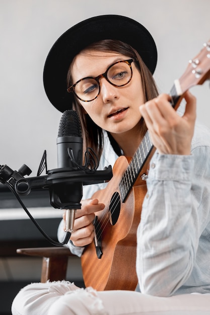 caucasian millennial woman in a hat with a microphone, playing guitar or ukulele