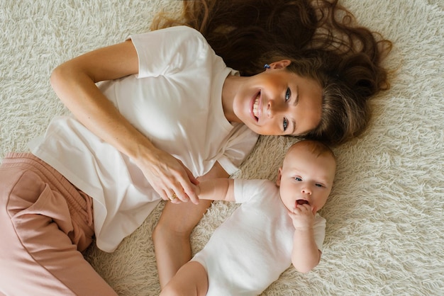 Caucasian mom lies on the bed with her baby son and smiles happily Top view of the family