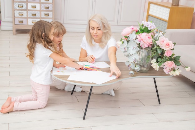 Caucasian Mother and kid girl draw together sitting on the floor in the living room. Happy family concept.