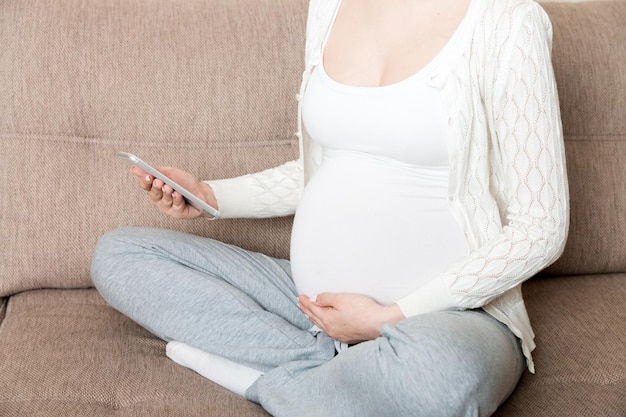 Caucasian pregnant girl using cellphone resting on bed in home