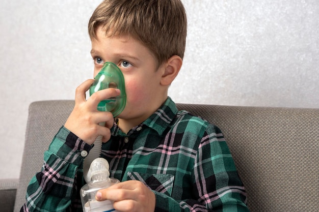 Caucasian preschooler boy uses a nebulizer sitting at home on the sofa