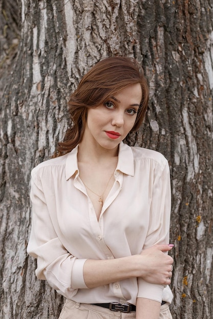 Caucasian pretty girl with red lips curly hair in stylish beige blouse outdoors