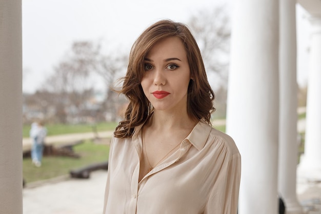 Caucasian pretty woman with red lips, wavy hair in stylish beige blouse outdoors