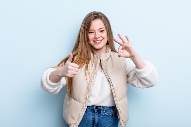 Caucasian red hair woman feeling happy, amazed, satisfied and surprised, showing okay and thumbs up gestures, smiling