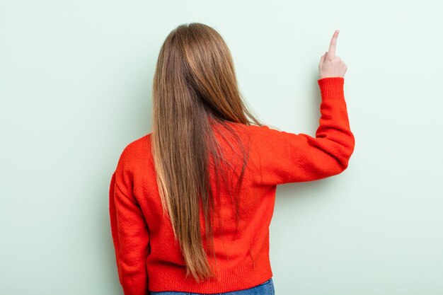 Photo caucasian red hair woman standing and pointing to object on copy space, rear view