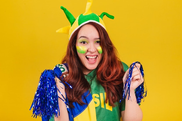 Caucasian redhaired woman soccer fan from brazil dancing wearing cheerleader pom poms