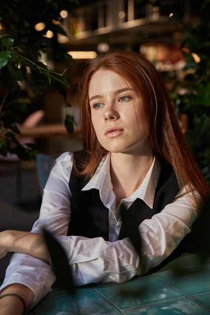 Caucasian redhead pretty girl with long hair sitting at coffee shop table