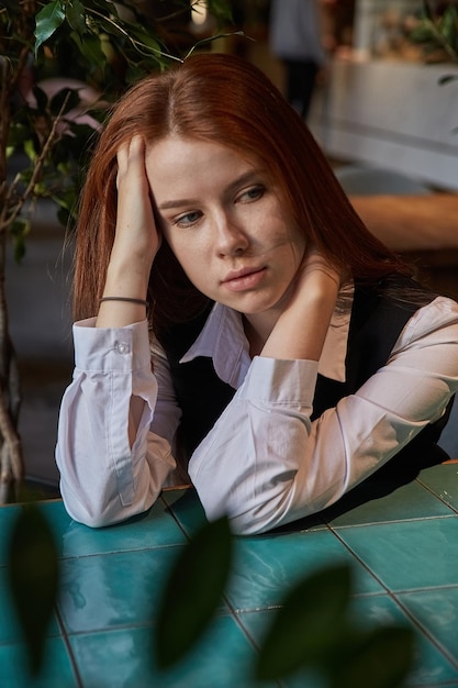 Caucasian redhead pretty girl with long hair sitting at coffee shop table