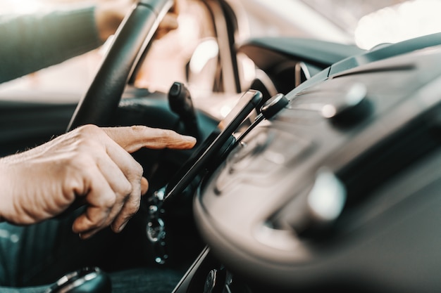 Caucasian senior man turning on navigation on smart phone while sitting in his car.