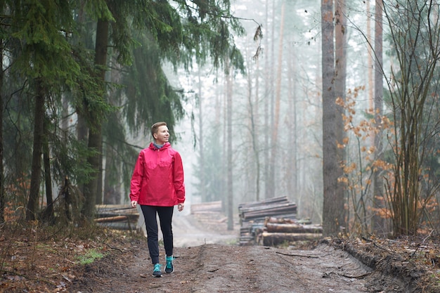 Caucasian short-haired, weared in pink raincoat smiling woman walking in foggy forest