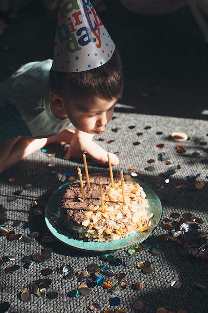 Caucasian small boy wearing a party cap is blowing the lights on the cake celebrating birthday