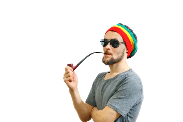 caucasian smoker man in rasta hat sunglasses and grey tshirt on white background with smoke pipe