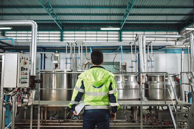 Caucasian technician engineer man in safety uniform standing with pipeline boiler tank in beverage processing laboratory plant