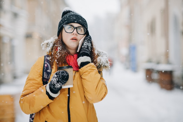 Caucasian teenage woman talking on the phone laughing holding a takeaway coffee cup smiling. Outdoors winter portrait of beautiful teenage girl speaking on the phone