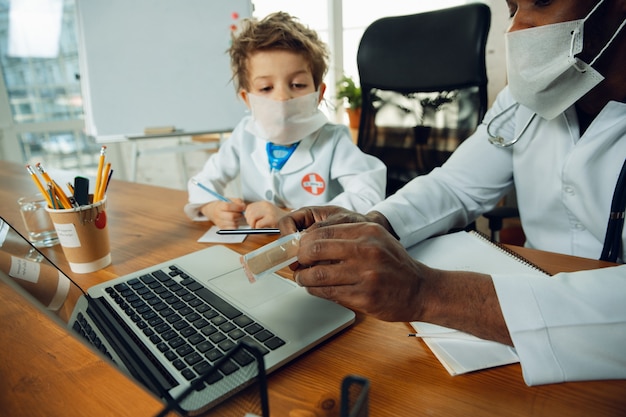 Caucasian teenboy as a doctor consulting, giving recommendation, treating. Little doctor during discussing, studying with older colleague. Concept of childhood, human emotions, health, medicine.