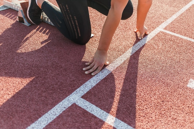 Caucasian woman at the athletic track starting point hands on the start line and legs