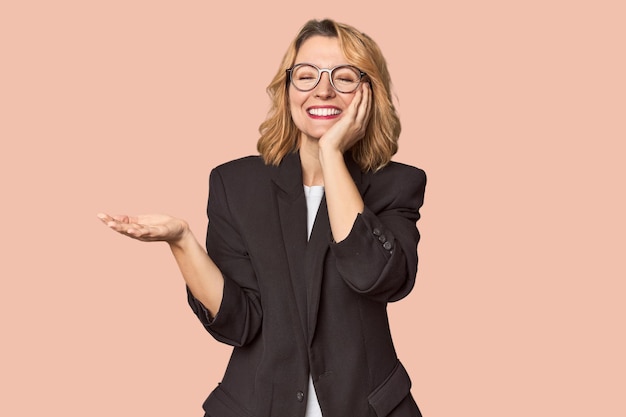 Photo caucasian woman in black business suit holds copy space on a palm keep hand over cheek amazed