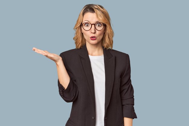 Caucasian woman in black business suit impressed holding copy space on palm