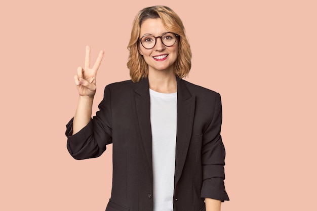 Caucasian woman in black business suit joyful and carefree showing a peace symbol with fingers