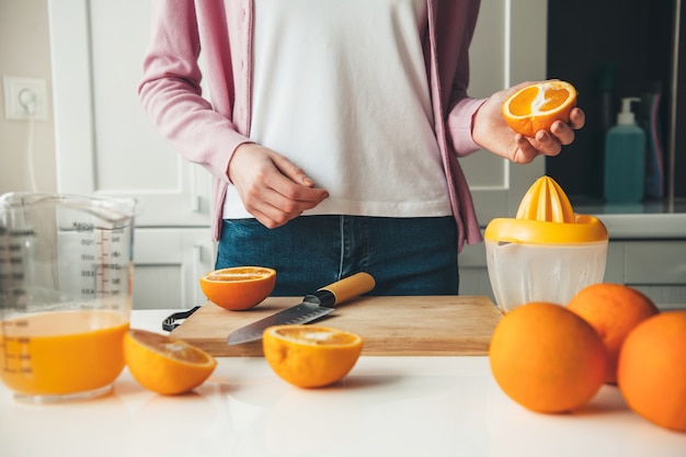 Caucasian woman in casual clothes is slicing fruits and making juice at home in the kitchen