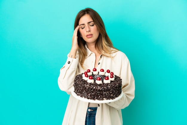 Caucasian woman holding birthday cake isolated on blue background with headache