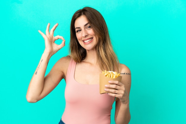 Caucasian woman holding fried chips isolated on blue background showing ok sign with fingers