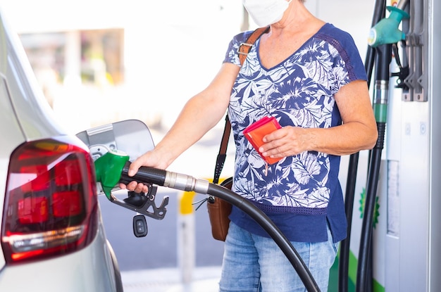 Caucasian woman holding petrol gasoline fuel pump to refuel her silver car at service station