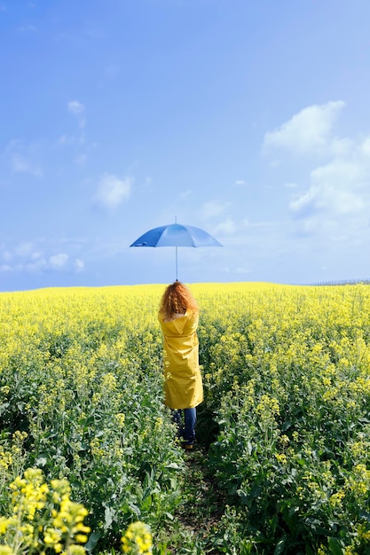 Caucasian woman holding an umbrella in a beautiful yellow field on a rainy summer day