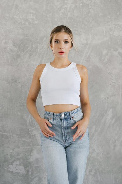 Photo caucasian woman is wearing a white top and blue jeans she stands against a grey background in the studio