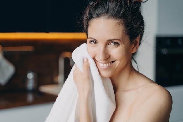 Caucasian woman is wiping face with towel and smiling Hygiene dermatology and skin cleansing