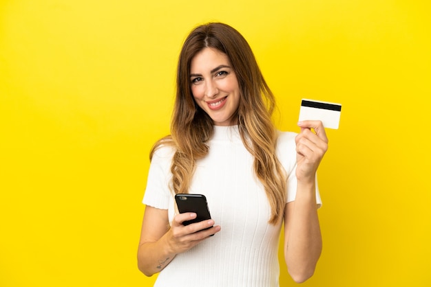 Caucasian woman isolated on yellow background buying with the mobile with a credit card